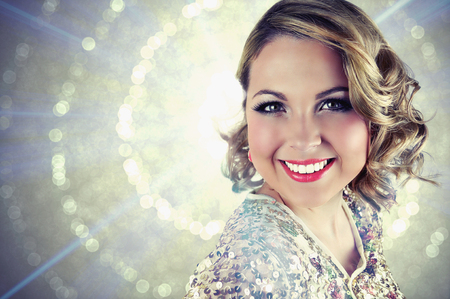 Blonde smiling woman with short curly hair wearing evening makeup and a sparkling sequin bolero on glittering background.の写真素材