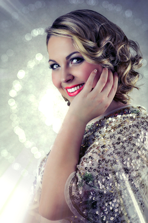 Blonde smiling woman with short curly hair wearing evening makeup and a sparkling sequin bolero on glittering background.の写真素材