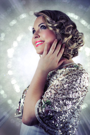 Blonde smiling woman with short curly hair wearing evening makeup and a sparkling sequin bolero on glittering background.の写真素材