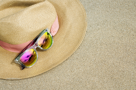 Brown straw summer hat and pink sunglasses on the sand at the beach.の写真素材