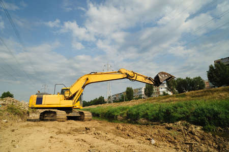 Crawler excavator at work. Lateral view of big crawler excavator on riverbed site in town district.