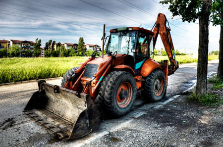 Excavator parked on the street. Big excavator parked at the tree shadow on the highway.