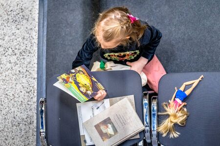 VILNIUS, LITHUANIA - FEBRUARY 24, 2019: The international Vilnius Book Fair. Little girl is reading a book about big data. On the chairのeditorial素材