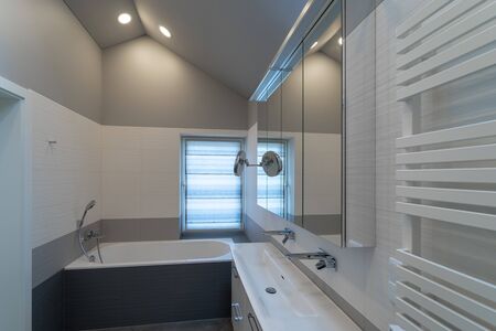 The interior of a modern bathroom with a window in a private house. Bath, cabinets with mirror and...