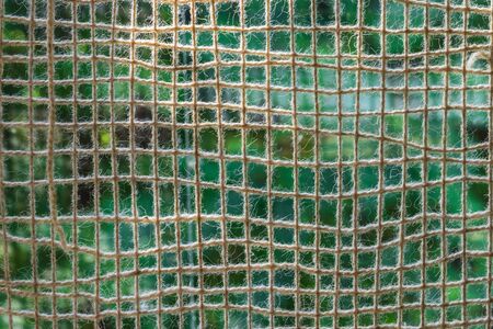 Cotton net of thick yarn outdoor. The mesh is against light. The background - a green meadow