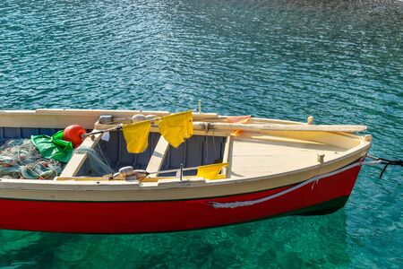 Part of a small fishing boat painted in bright red, beige and green colors in the blue water of the...