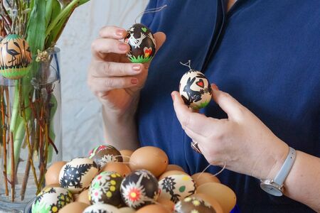 Female hands holding colorfully decorated Easter eggs with paper cuttings. Natural and patterned eggs placed on the front. A vase with a bouquet and an egg on the left. Selective focus, close-upの写真素材