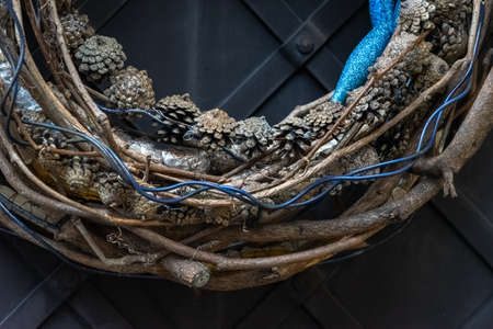 Detail of a modern Advent wreath hung on a metal exterior door. Minimalist unconventional design. Natural (twigs, wicker, pine cones) and artificial materials (glitter, plastic, wire) used. Close upの写真素材