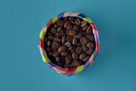 Roasted coffee beans spilling out of a colorful basket on a blue backgroundの写真素材
