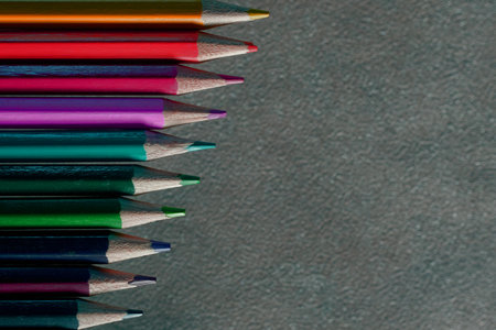 Colored pencils in a variety of bright shades are meticulously arranged in a row on a textured surface, perfect for artists or creative projects. The vibrant colors invite inspiration.の写真素材