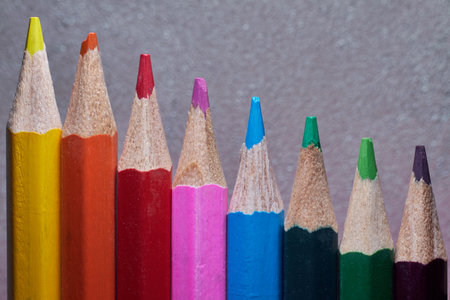 Colored pencils in a variety of bright shades are meticulously arranged in a row on a textured surface, perfect for artists or creative projects. The vibrant colors invite inspiration.の写真素材