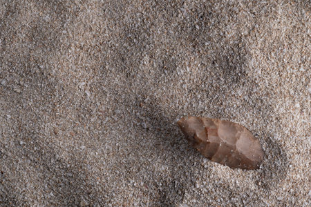 A carefully shaped flint spear-head tool shows evidence of ancient craftsmanship and reflects early human activities such as hunting and gathering in a prehistoric context, shown on a sandy background.の写真素材