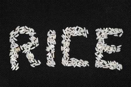 Artistic image featuring the word "RICE" spelled out using white rice grains on a textured black background, highlighting creativity and simplicity.の写真素材