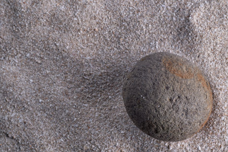 Close-up view of a textured volcanic rock on a sandy background. The natural formation demonstrates the geological processes involved in its creation.の写真素材