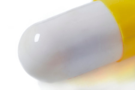 A yellow and white medicine capsule in a macro close-up on a white background, related to topics of medicine, pharmacology, health and personal care.の写真素材