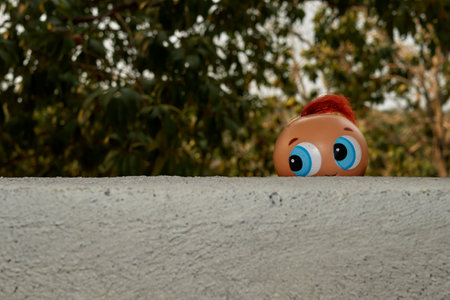 Playful Toy Head Peeking Over a Wall Amidst a Nature Backdropの写真素材