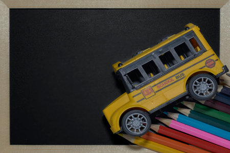 Yellow Toy School Bus on Colored Pencils and Blackboard Background