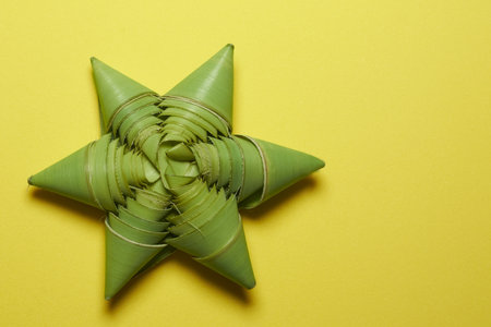 Close-Up of Green Woven Star Craft on Bright Yellow Surfaceの写真素材