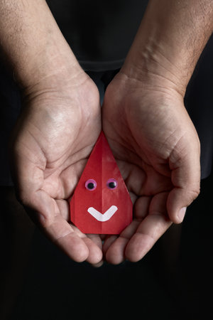 An origami drop of blood remains in open hands in an act of offering, symbolizing blood donation.の写真素材
