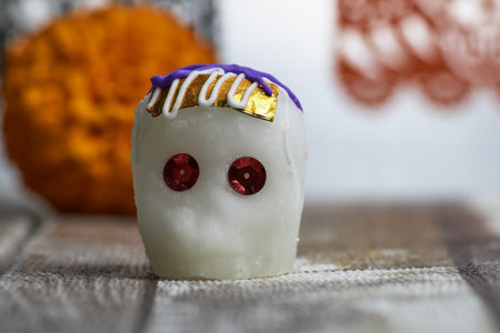 A white sugar skull decorated as a ghost with a background of a bright orange marigold flower.