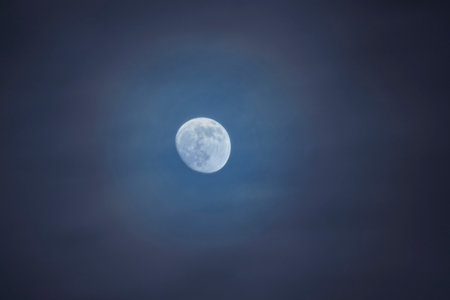 A serene night scene featuring a pale full moon surrounded by wispy blue clouds. The tranquil atmosphere evokes quiet reflection, wonder, and the beauty of the natural sky above.の写真素材