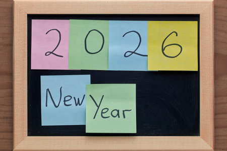 A wooden framed chalkboard displays 2026 with pastel Post It notes spelling out New Year, creating a...