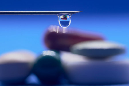 A detailed macro shot showing a balanced drop of liquid on the tip of a needle, reflecting medicinal...