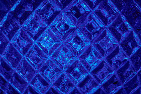 Macro photograph of a blue glass surface with geometric relief and flashes of cold light.の写真素材