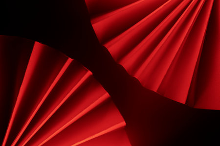 Pleated paper arranged dynamically, highlighted by side lighting in red tones.の写真素材