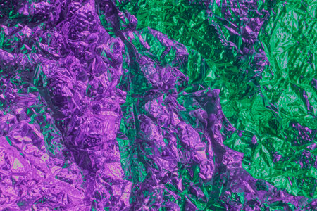 A vivid close-up of purple and green crumpled foil creates a bold, reflective texture perfect for...