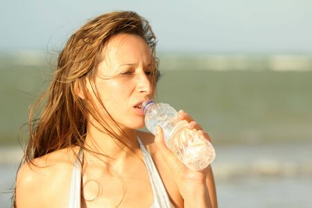 woman drinking water on the beach by sunset