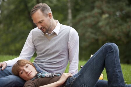 young woman relaxing on a male leg in city parkの写真素材