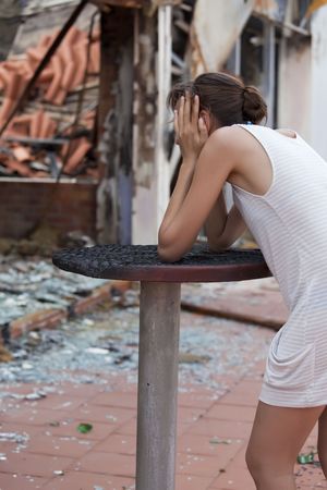 pained woman stands in front of burned out houseの写真素材