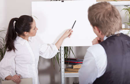 woman pointing with a pen on white billboard in office