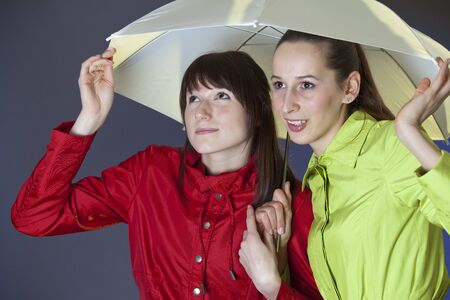 two women in coats holding umbrella and running from rainの写真素材