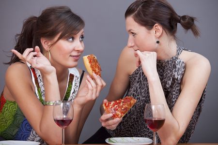 two female friends talking in studio with glasses sparkling wine and pizzasの写真素材