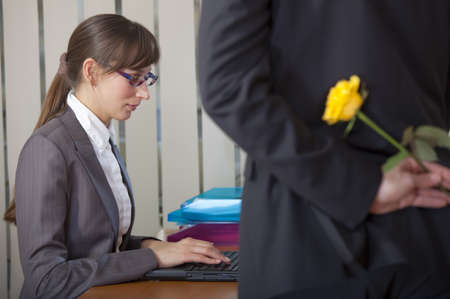 romantic scene in office - man wants surprise woman with flowerの写真素材