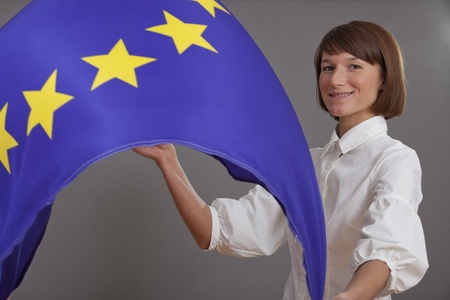 happy woman waving european flag over grey background (flash spot on at the right side above should accent the cheerful character of the image)の写真素材