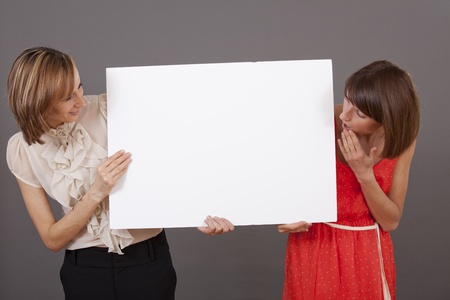 two happy and surprised women holding a white banner over grey backgroundの写真素材
