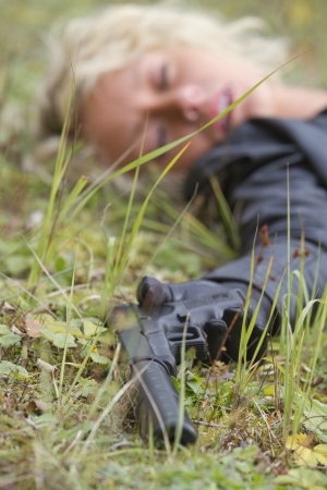 Crime scene - woman playing dead scene with a silencer handgun in her hand, focus on the gunの写真素材