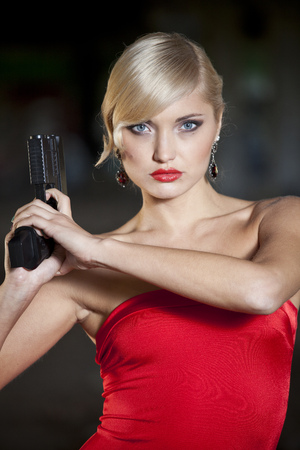 woman in retro look and red dress holding a handgunの写真素材