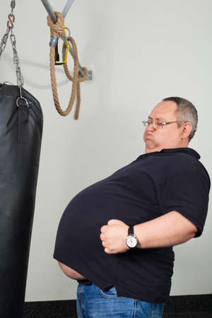 Fat man match belly with a punching bag in the gymの写真素材