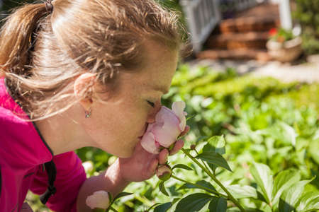 Young beautiful woman enjoying scent of a rose blooming in the gardenの写真素材