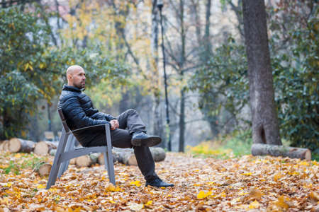 Young man sitting on a bench in a park in autumnの写真素材