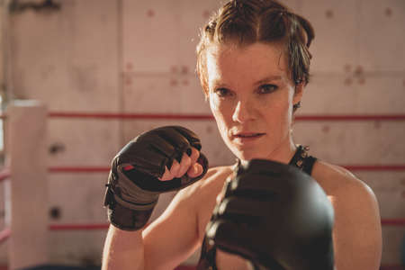 Gorgeous woman, mma fighter in gym during training. Preparing for a hard caged match. Sexy fighter girl punching actively. Aggressive and ready to fight.の写真素材