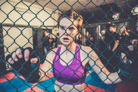 Gorgeous woman, mma fighter in gym during training. Preparing for a hard caged match. Sexy fighter girl punching actively. Aggressive and ready to fight.の写真素材