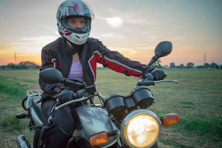 young attractive woman whith motorcycle outdoors on dirt road at sunriceの写真素材