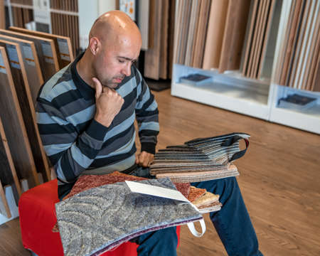 the man chooses the color of the new carpet according to the samples in the flooring shop