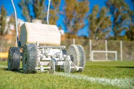 Splashing white paint on the grass to help the machine to mark the boundaries of a football field.