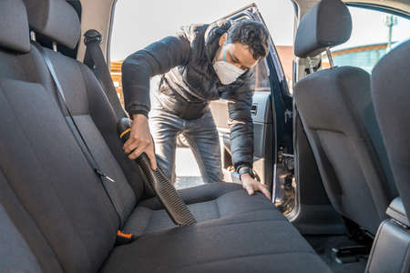 vacuuming the interior of a car with a respirator on the face during a coronavirus epidemic
